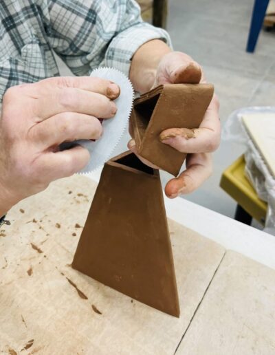 Close up of hands assembling slab built triangle vase, scoring with metal rib