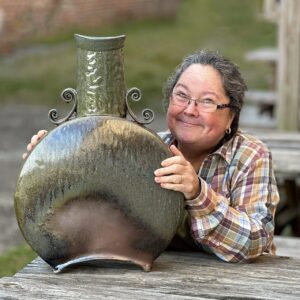 Karen Dubois sitting with large hand built finished pot, wood soda kazie fired