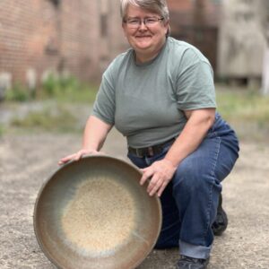 Julia Mann kneeling with her finished pot, large bowl, smiling