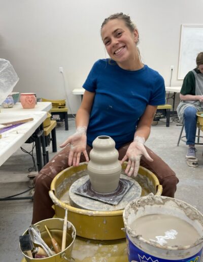 TVP Teaching Center Class student throwing at the wheel, Intermediate wheel Class, smiling showing off her pot